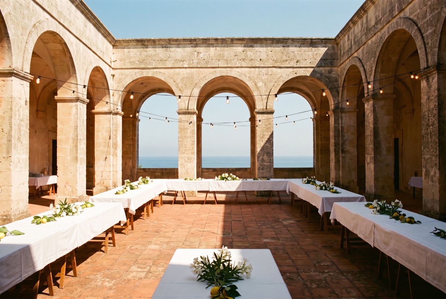 A seafront courtyard with limestone arches and long laid tables, taken before any guests arrived.