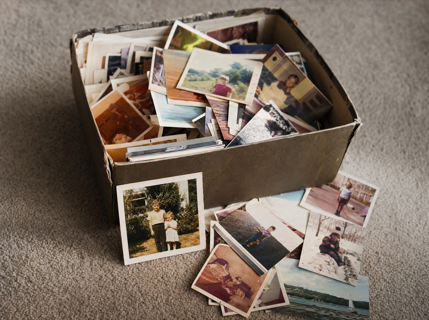 A shoebox of loose prints and paper wallets of negatives, opened on a carpet.